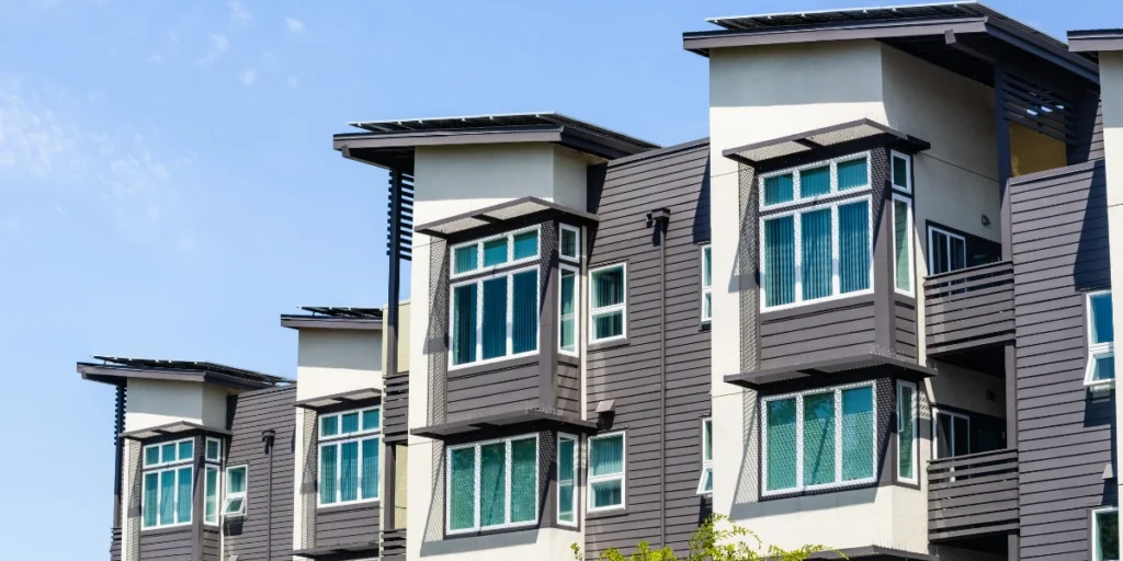 Modern apartment building with large, geometric windows and gray siding set against a clear blue sky.