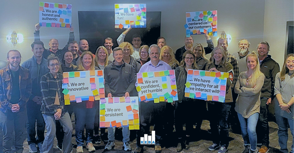 A group of people smiling indoors, holding colorful signs with positive phrases like We are innovative and We are fun, surrounded by sticky notes.