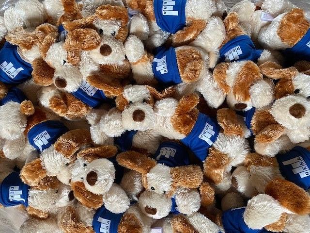 A pile of brown and white plush dog toys wearing blue shirts with a white rectangular logo on them—all closely packed together—resembles a cozy cluster, much like a well-organized set of data arranged for easy access.