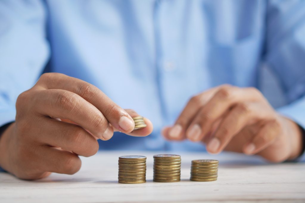 A person in a blue shirt stacks coins into neat piles on a white table, with one hand holding a small stack and the other arranging coins.