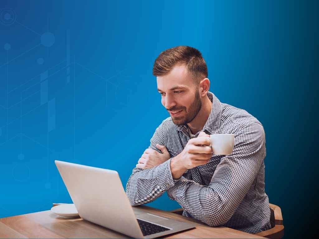 Man in a checkered shirt sits at a table, smiling while holding a white mug and looking at a laptop. The background is blue with subtle graphic patterns.