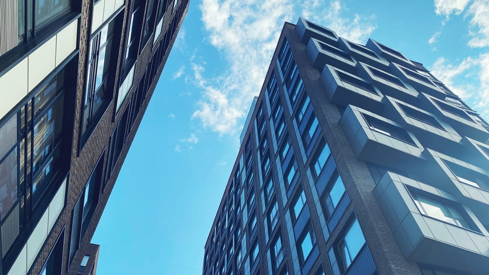 Two modern high-rise buildings are shown from a low angle, with a bright blue sky and some clouds in the background, highlighting the architectural expertise of their operators.